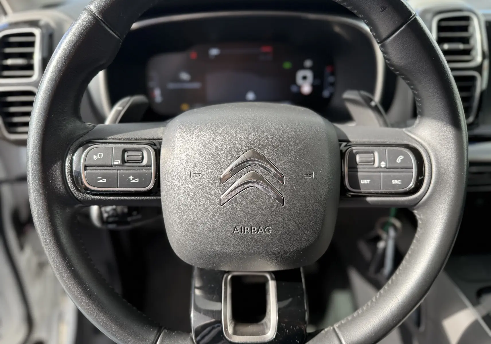 Vue rapprochée du volant noir de la Citroën C5 Aircross 2021 avec commandes intégrées et logo chromé central.