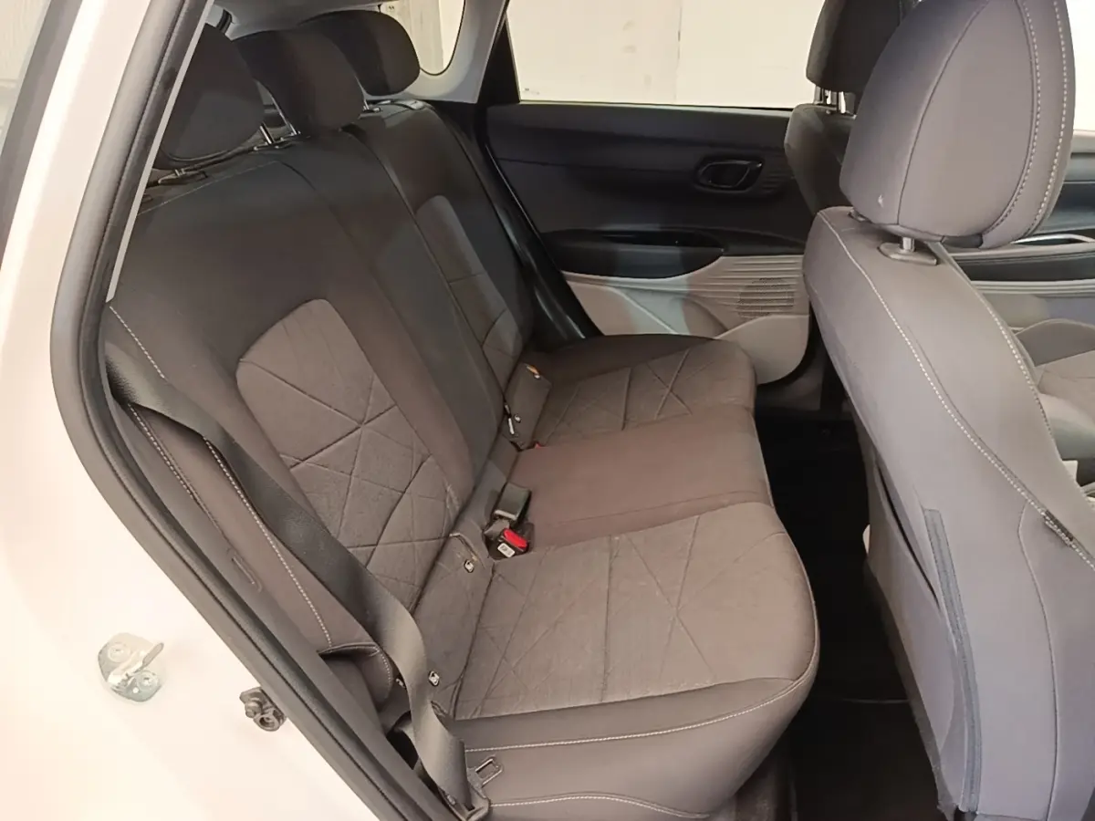 Vue intérieure côté gauche montrant la banquette arrière grise du Hyundai Bayon blanc 2024 avec ceinture de sécurité.
