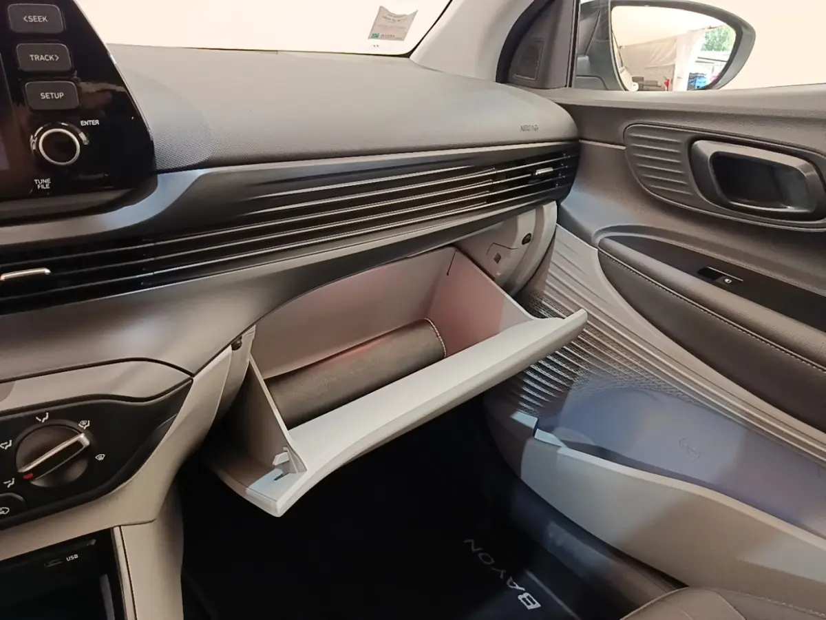 Intérieur côté passager de la Hyundai Bayon 2024, boîte à gants ouverte et tableau de bord noir et gris.