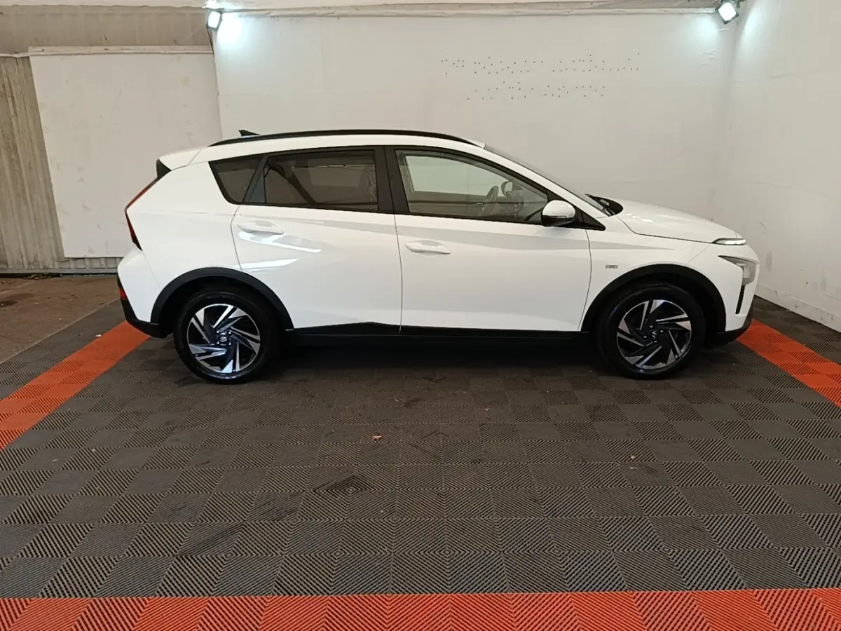 Vue de profil côté droit d'un Hyundai Bayon blanc 2024 avec jantes alliage et toit noir dans un garage.