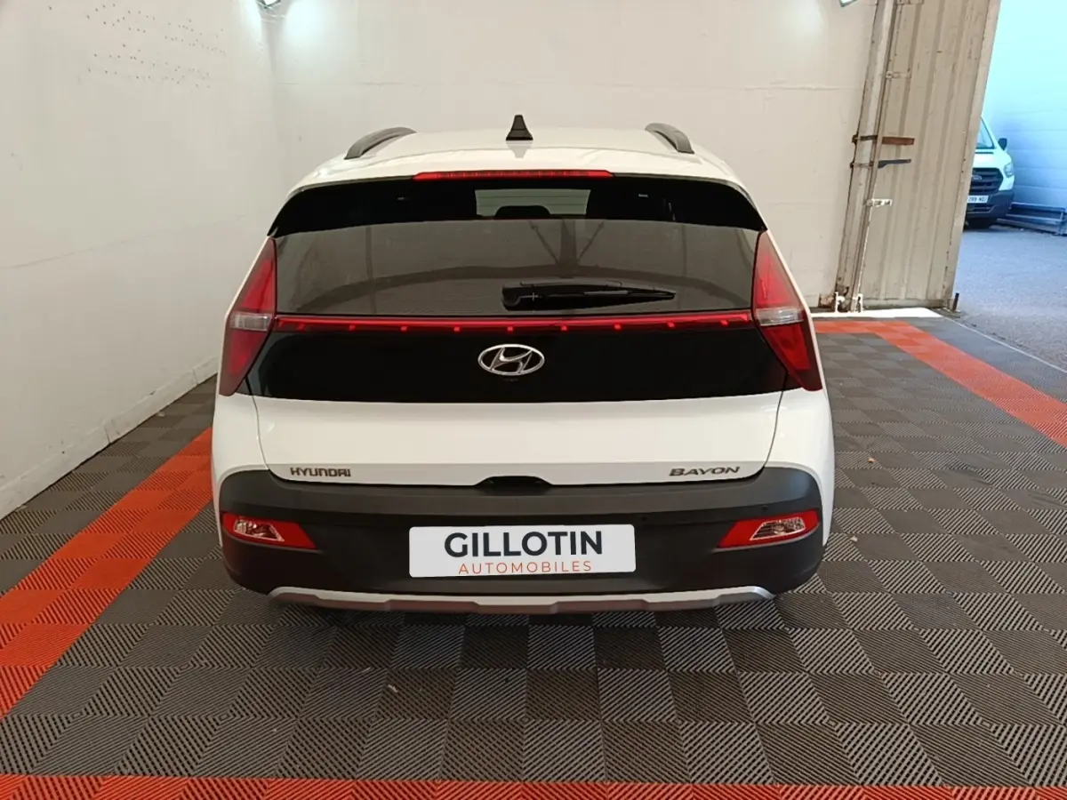 Vue arrière d'une Hyundai Bayon blanche 2024 avec feux arrière reliés par une bande lumineuse rouge.