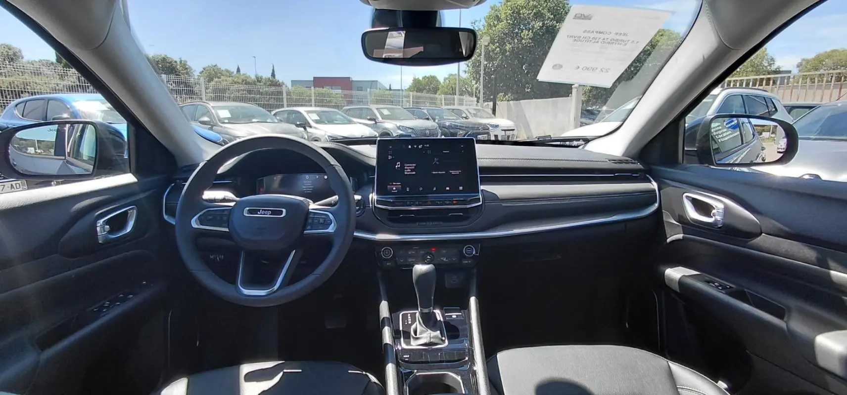 Vue intérieure avant du Jeep Compass 2025 avec tableau de bord noir, écran tactile et volant multifonction.