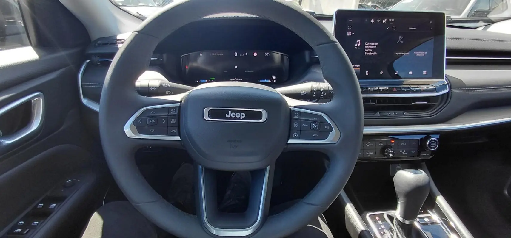 Vue intérieure centrée sur le volant Jeep noir et l’écran tactile du tableau de bord du Compass 2025.