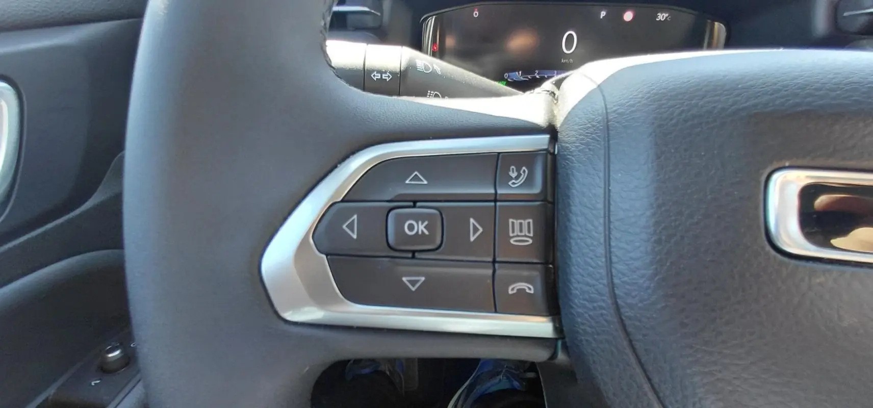 Gros plan sur les commandes gauche du volant en cuir noir du Jeep Compass bleu 2025, affichage numérique en arrière-plan.