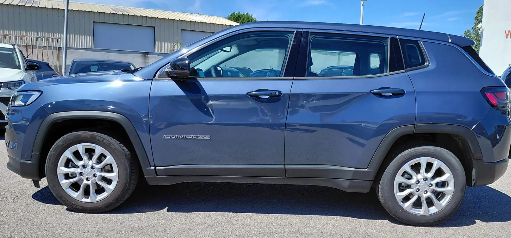 Vue de profil côté gauche d’un Jeep Compass bleu 2025 avec jantes alliage 18 pouces et logo visible sur la porte.