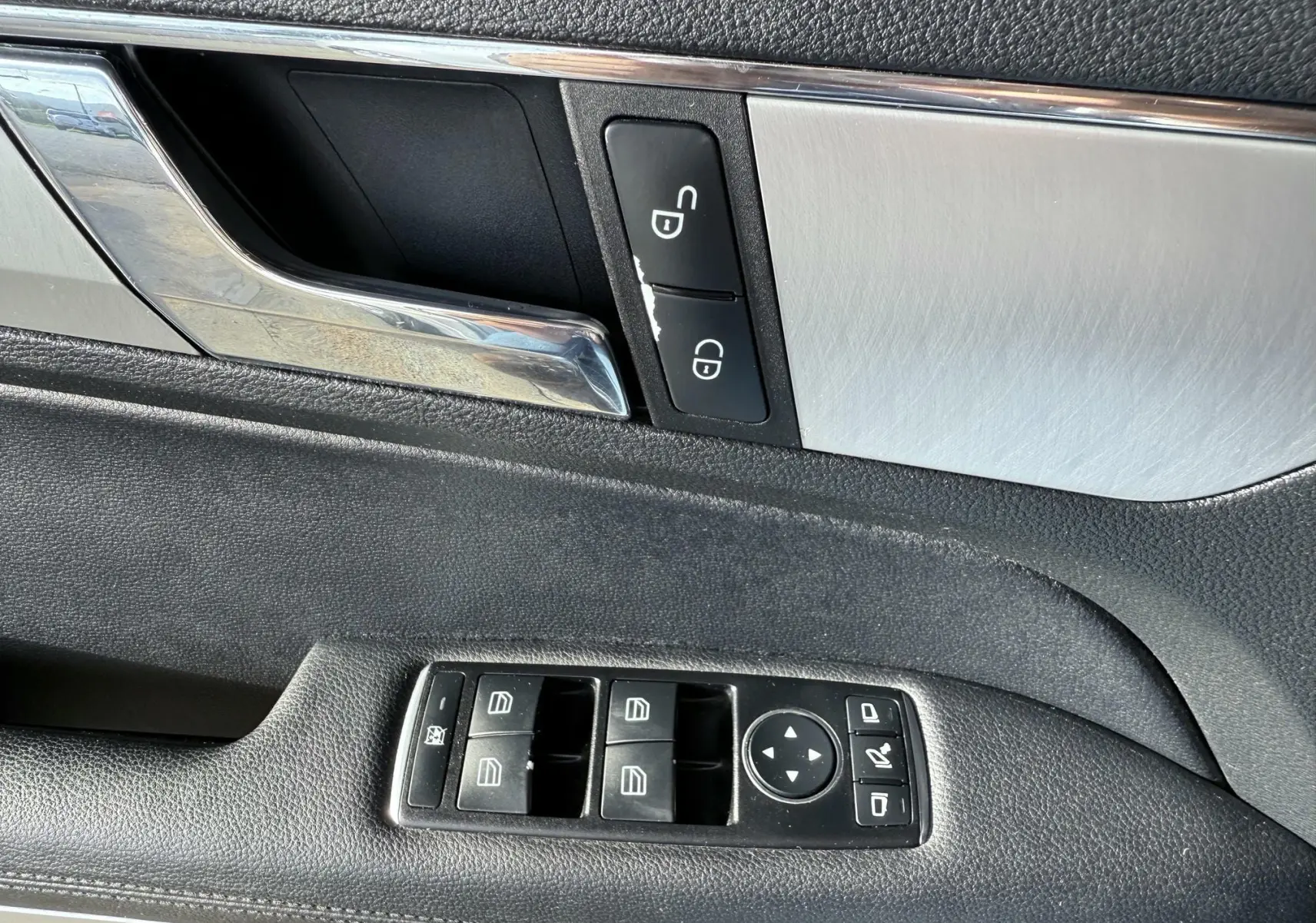 Gros plan sur la commande des vitres et la poignée intérieure côté gauche d'une Mercedes Classe E 250 Coupé gris.