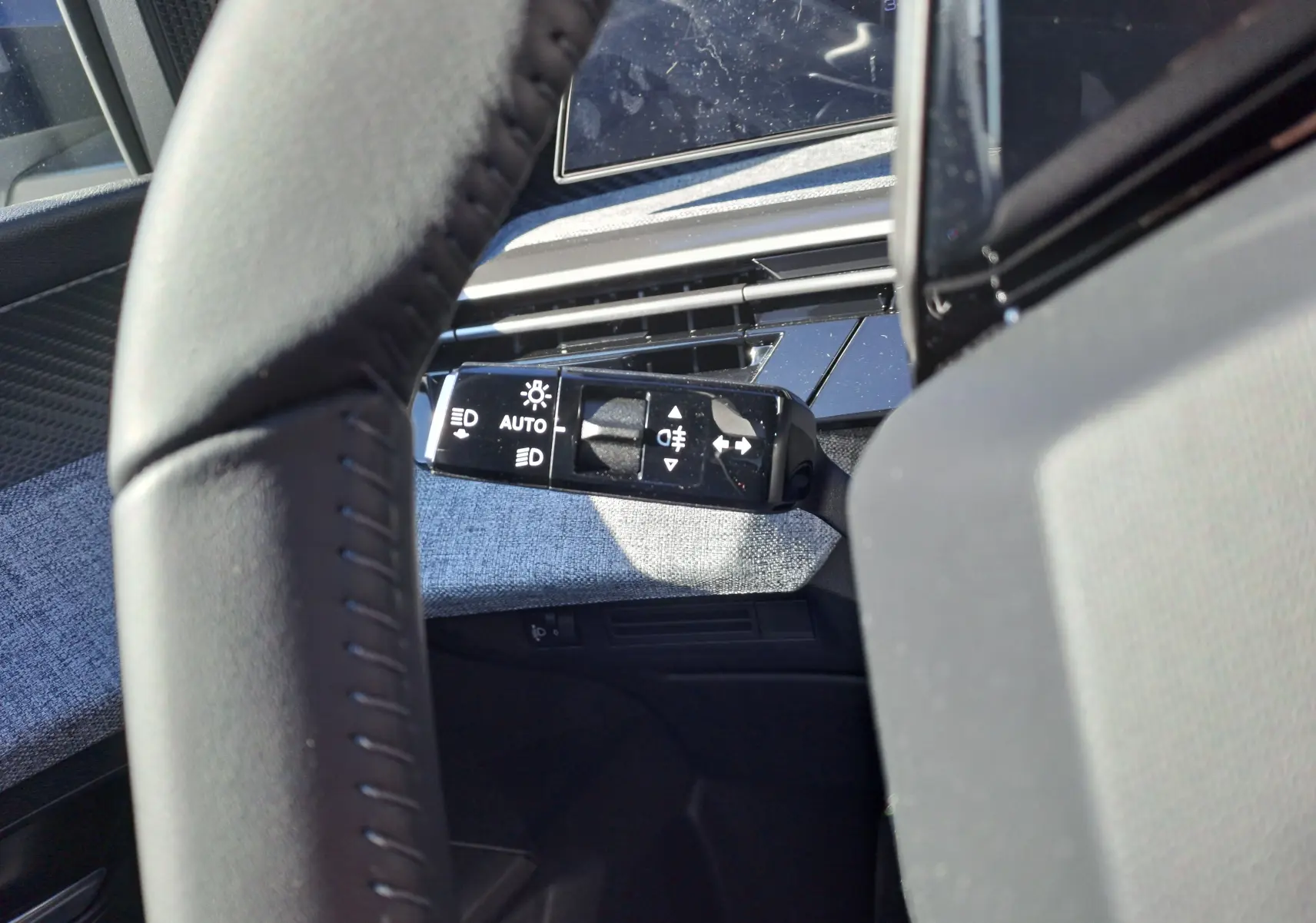 Gros plan sur la commande des phares à gauche du volant dans l'habitacle gris du Peugeot 3008 2024.