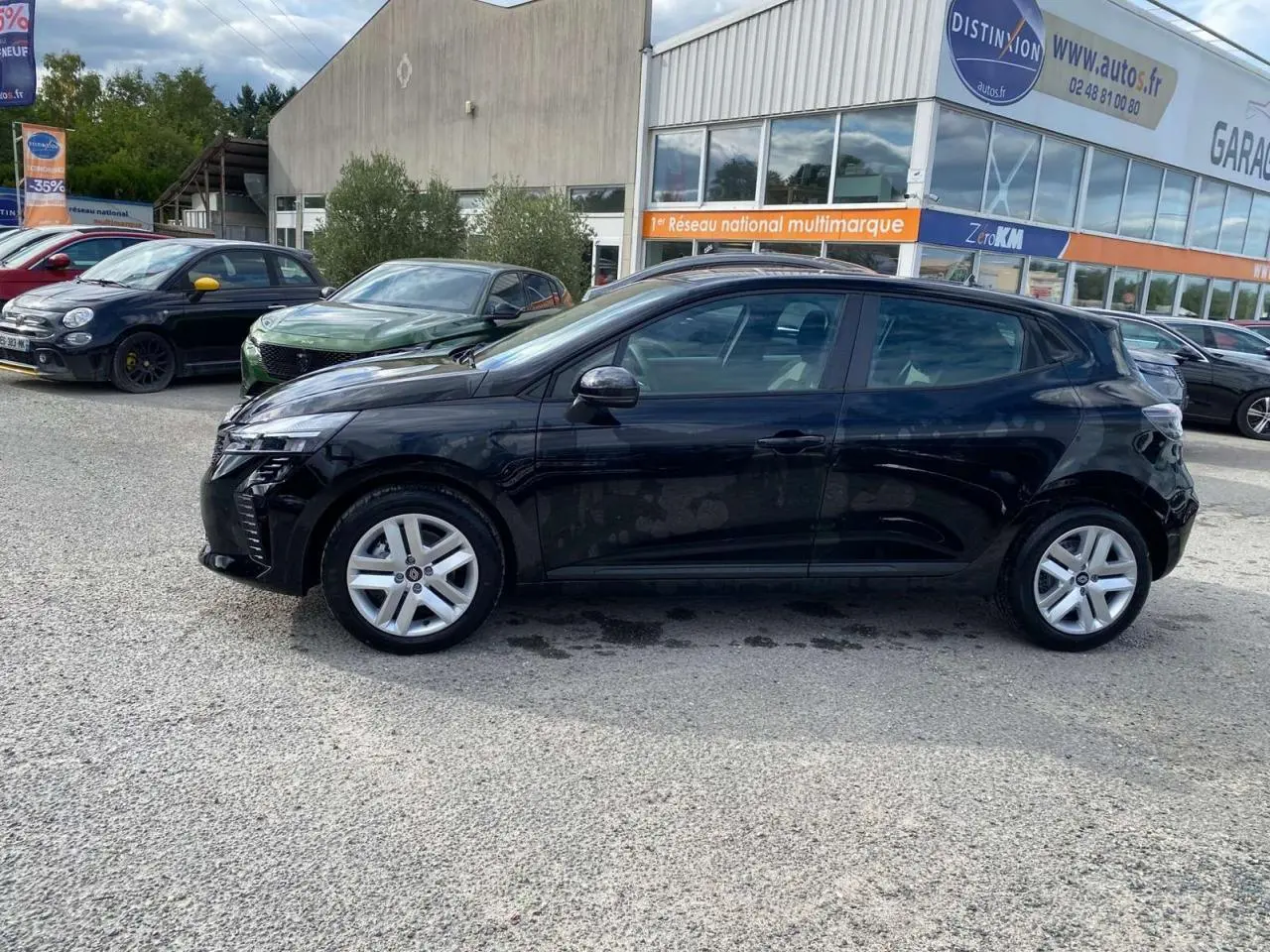 Profil côté gauche d'une Renault Clio 2025 noir étoilé garée devant un garage multimarque en extérieur.