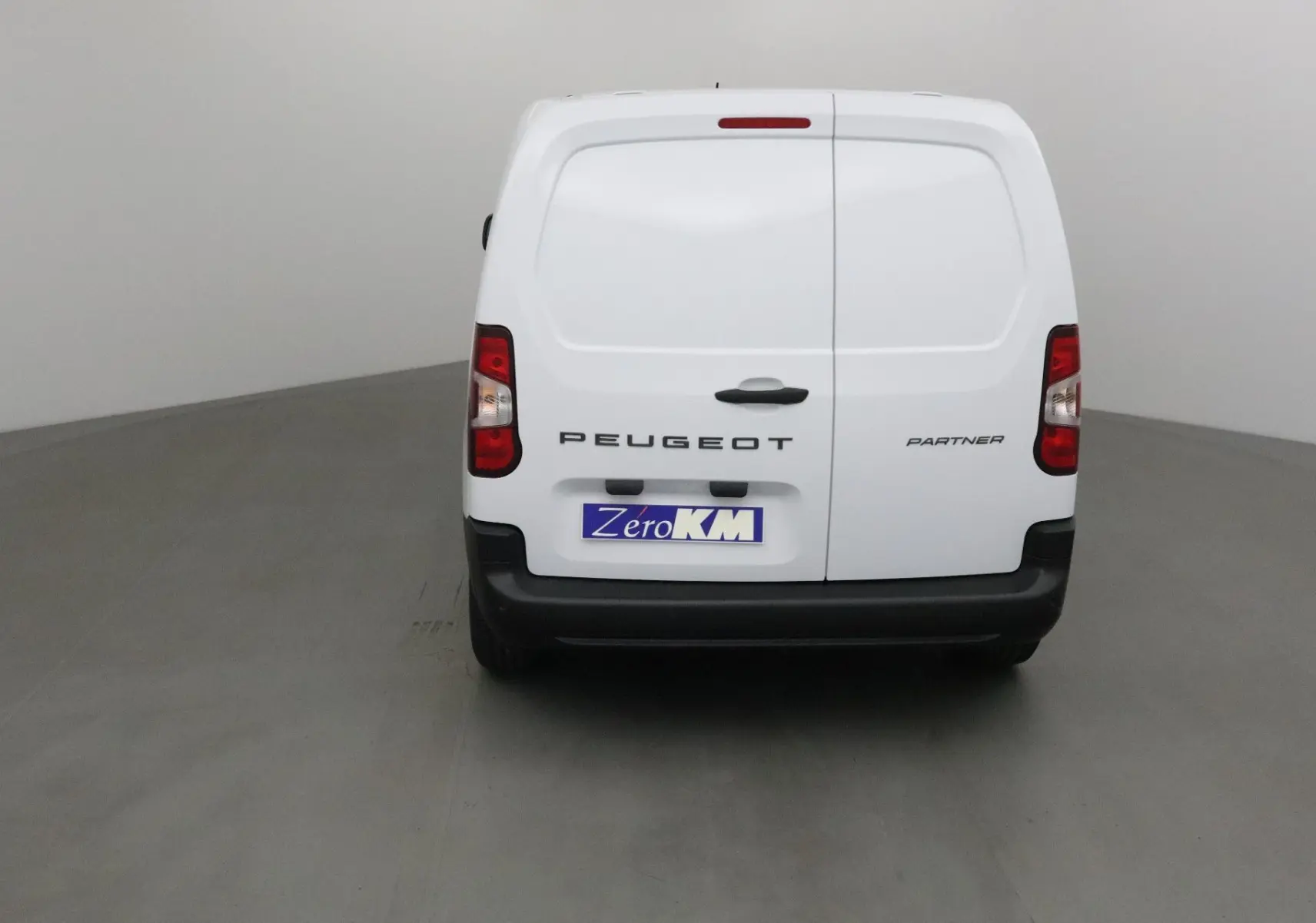 Vue arrière d’un utilitaire Peugeot Partner blanc avec portes battantes et plaque Zero KM visible.
