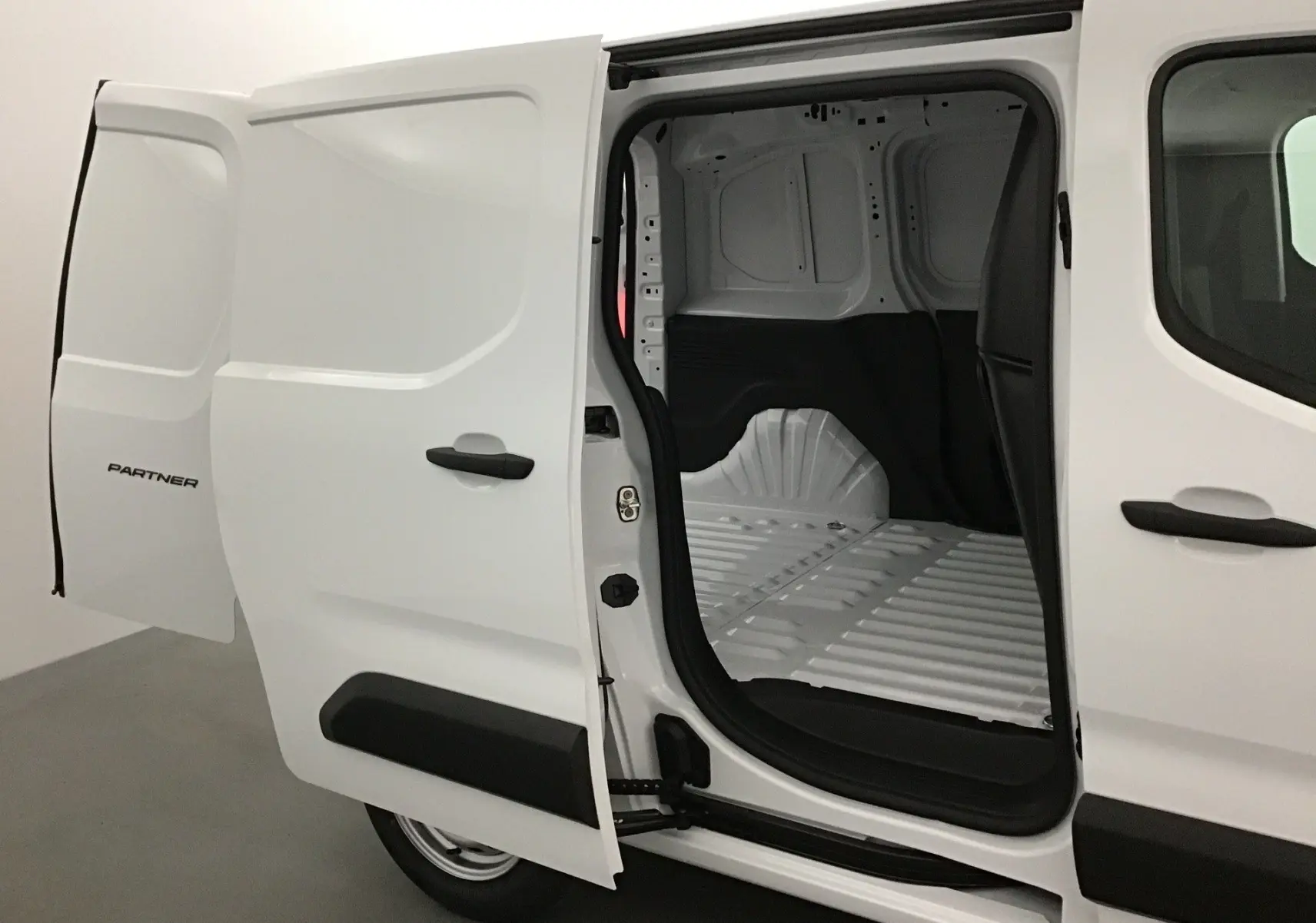 Vue latérale gauche du Peugeot Partner blanc 2025 avec porte coulissante ouverte dévoilant l’espace de chargement vide.