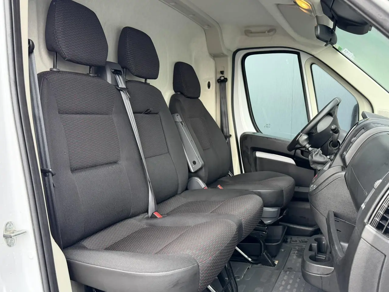 Vue intérieure côté conducteur de l'Opel Movano Fourgon blanc 2024, montrant les sièges avant en tissu noir et le tableau de bord.