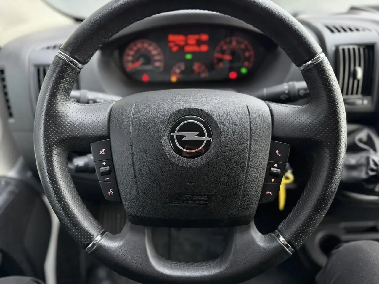 Vue rapprochée du volant en cuir noir de l'Opel Movano Fourgon 2024 avec tableau de bord flou en arrière-plan.