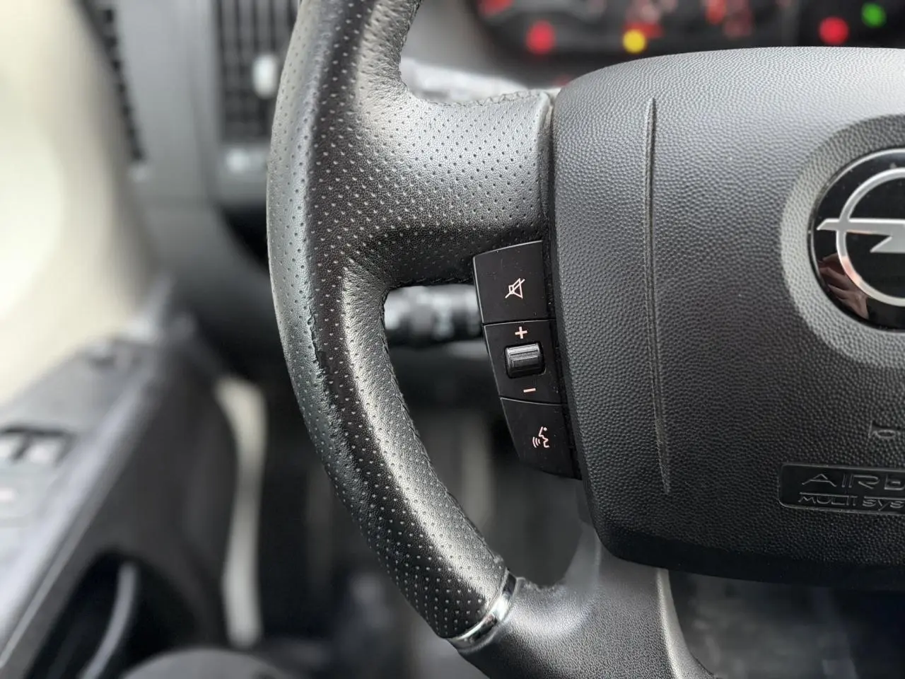 Gros plan sur le volant en cuir noir perforé de l'Opel Movano Fourgon 2024, avec commandes intégrées.