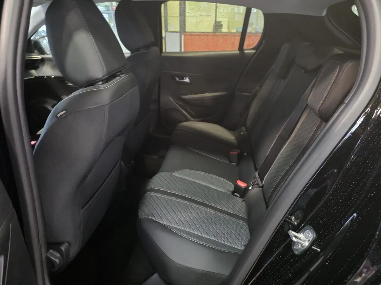 Vue intérieure arrière droite de la Peugeot 208 noire métallisée, montrant la banquette tissu bi-matière avec surpiqûres Quartz.