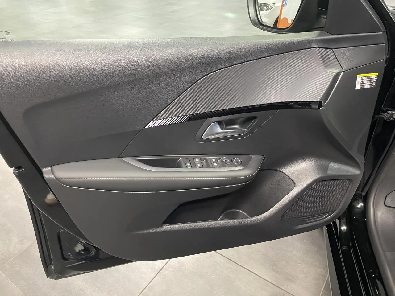 Vue intérieure de la porte avant gauche noire métallisée de la Peugeot 208 avec insert effet carbone et commandes électriques.
