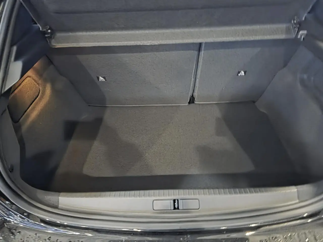 Coffre ouvert de la Peugeot 208 noire métallisée, montrant un espace de rangement propre et vide.