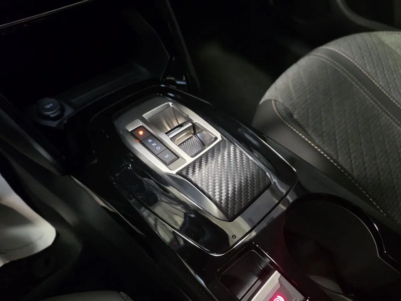 Vue rapprochée de la console centrale noire brillante avec levier de boîte automatique et sellerie tissu gris Peugeot 208 hybride 2025.