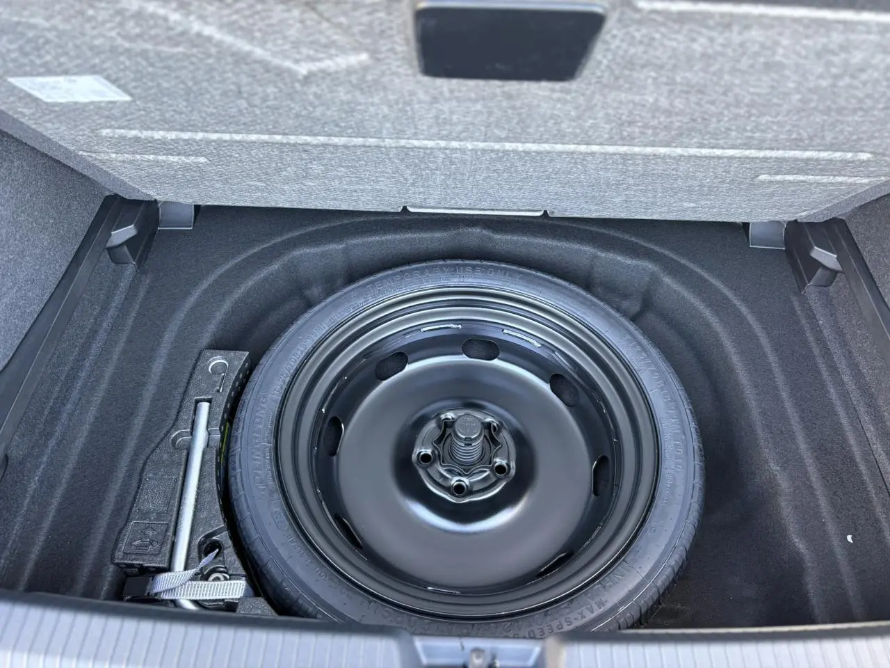 Vue plongeante sur la roue de secours noire dans le coffre d'une Volkswagen Golf VIII 2.0 TDI gris dauphin.