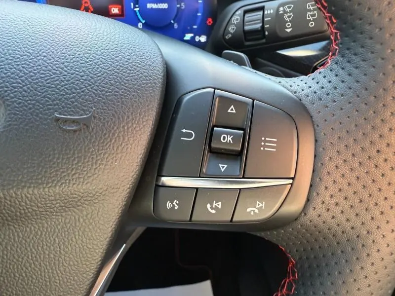 Gros plan sur les commandes multifonctions à droite du volant cuir perforé avec surpiqûres rouges du Ford Kuga noir Agate 2024.