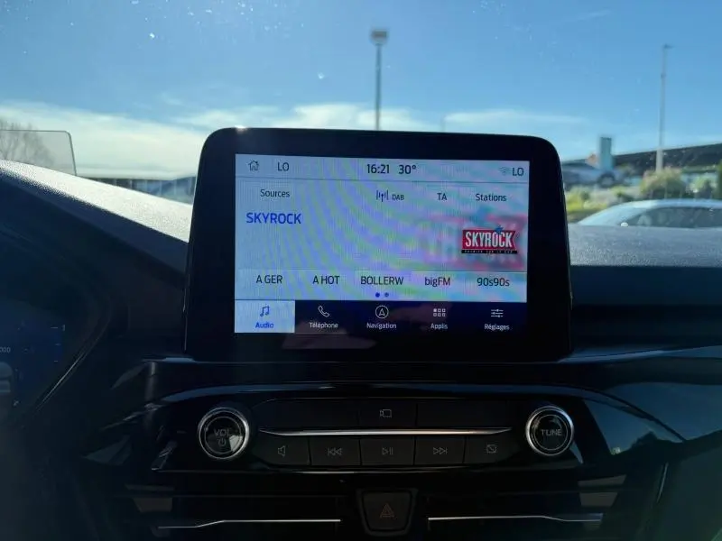 Écran tactile central du Ford Kuga 2024 affichant la radio Skyrock, avec commandes audio en dessous, vue intérieure avant.