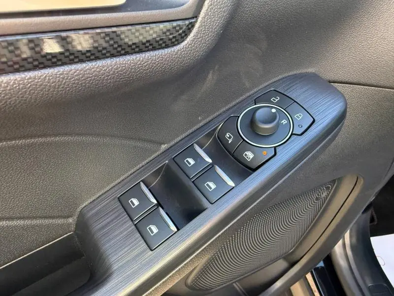 Gros plan sur la commande des vitres et rétroviseurs côté conducteur du Ford Kuga noir Agate Métallisée avec finition carbone.