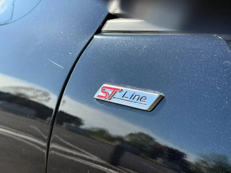 Gros plan sur l'emblème ST-Line sur la porte noire Agate métallisée d'un Ford Kuga 2024.