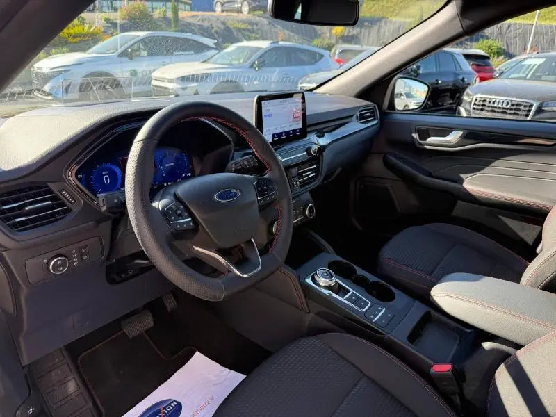 Vue intérieure côté conducteur du Ford Kuga 2024 noir, volant cuir multifonction et écran tactile central visible.