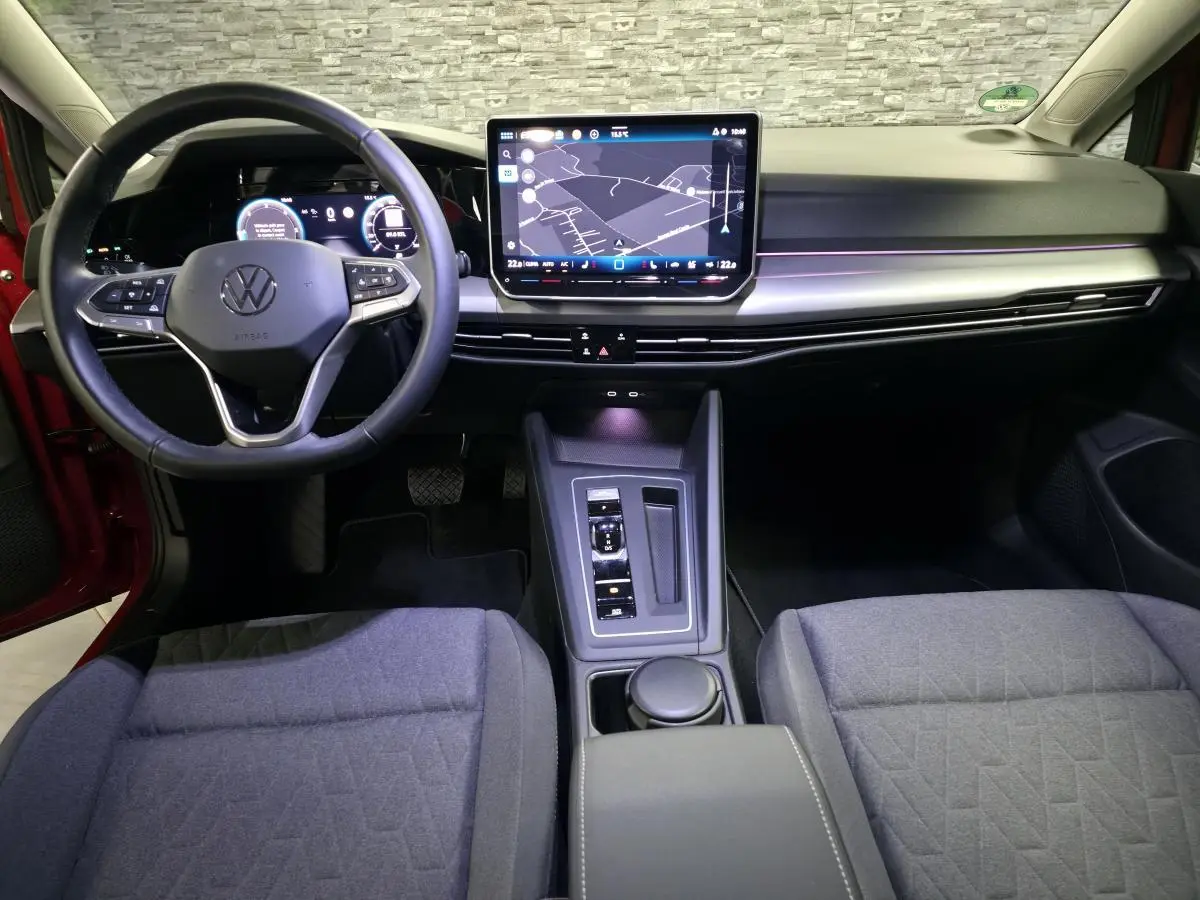 Vue intérieure avant de la Volkswagen Golf VIII rouge, tableau de bord moderne avec écran tactile central et volant multifonction.