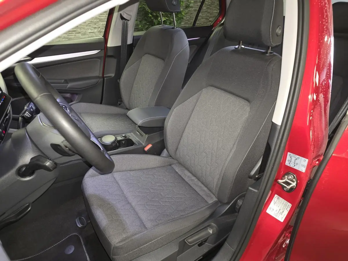 Vue intérieure côté gauche des sièges avant en tissu gris de la Volkswagen Golf VIII rouge métallisée avec accoudoir central.
