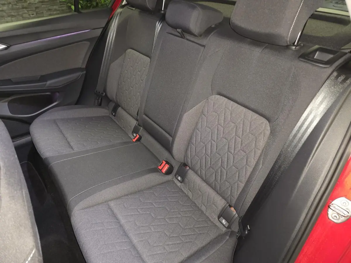 Vue intérieure sur la banquette arrière en tissu gris de la Volkswagen Golf VIII rouge, avec ceintures de sécurité visibles.