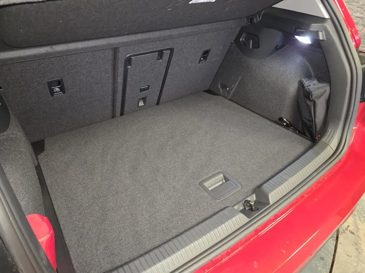 Coffre ouvert vu de dessus d’une Volkswagen Golf VIII rouge, avec tapis gris et éclairage intérieur allumé.