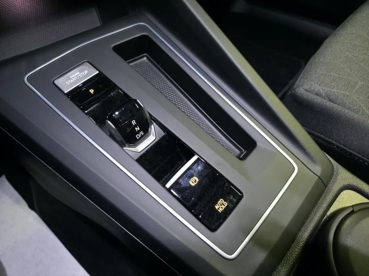 Gros plan sur la console centrale noire de la Volkswagen Golf VIII avec levier de vitesses automatique et bouton start/stop.