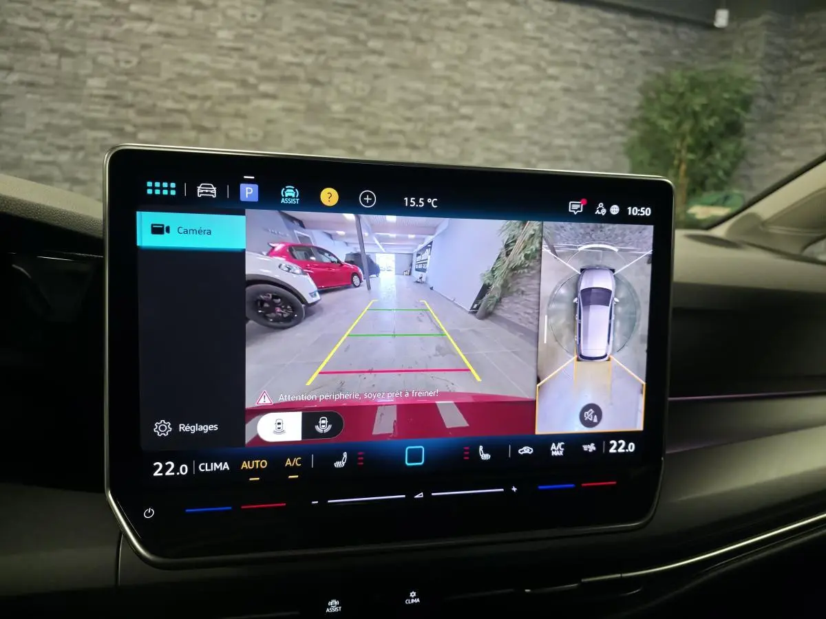 Écran central de la Volkswagen Golf VIII rouge montrant la caméra 360 et la vue arrière en stationnement intérieur.