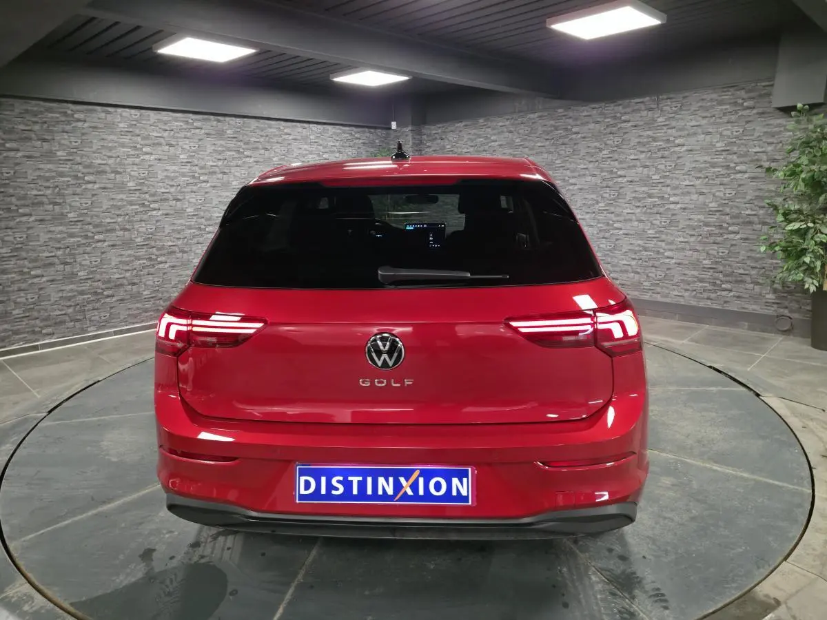 Vue arrière d'une Volkswagen Golf VIII rouge métallisé avec feux arrière LED allumés dans un showroom.