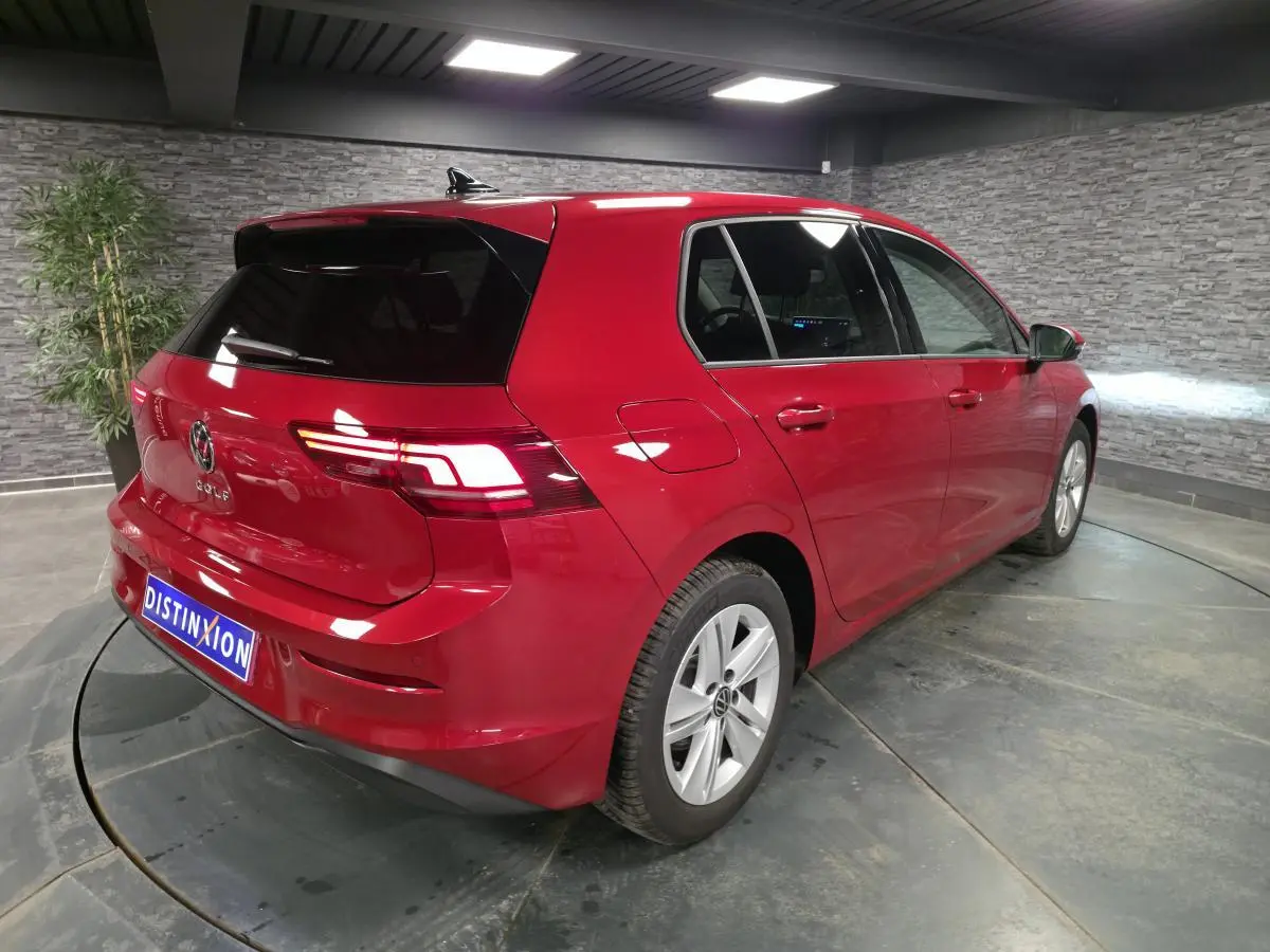 Volkswagen Golf VIII rouge métallisé vue 3/4 arrière droit avec feux arrière LED allumés en intérieur.