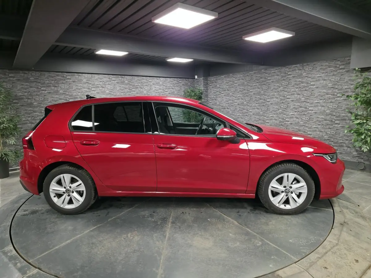 Volkswagen Golf VIII rouge métallisé vue de profil côté gauche en intérieur avec jantes alliage 16 pouces.
