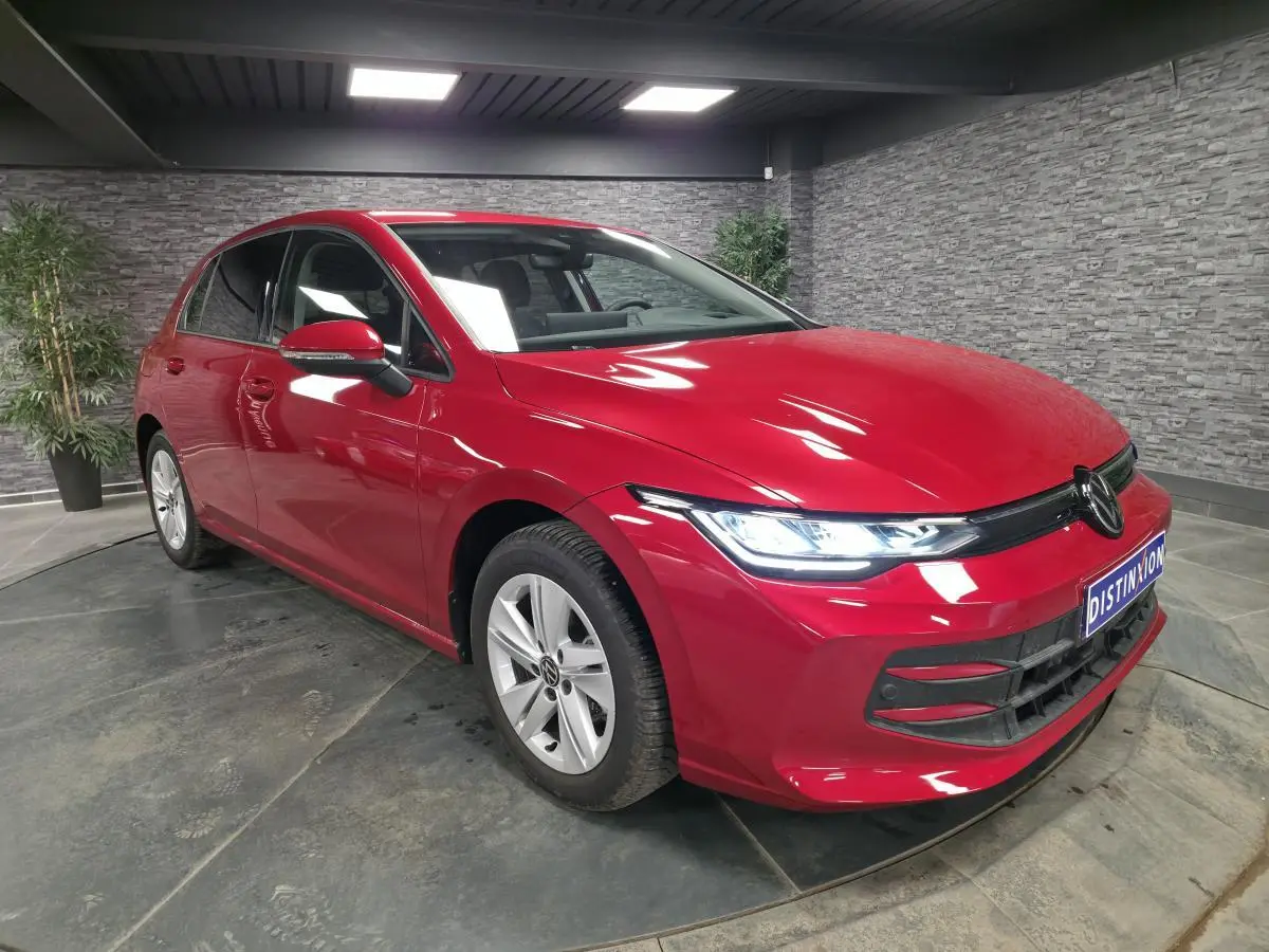 Volkswagen Golf VIII rouge métallisé vue 3/4 avant droit avec phares LED allumés en intérieur.