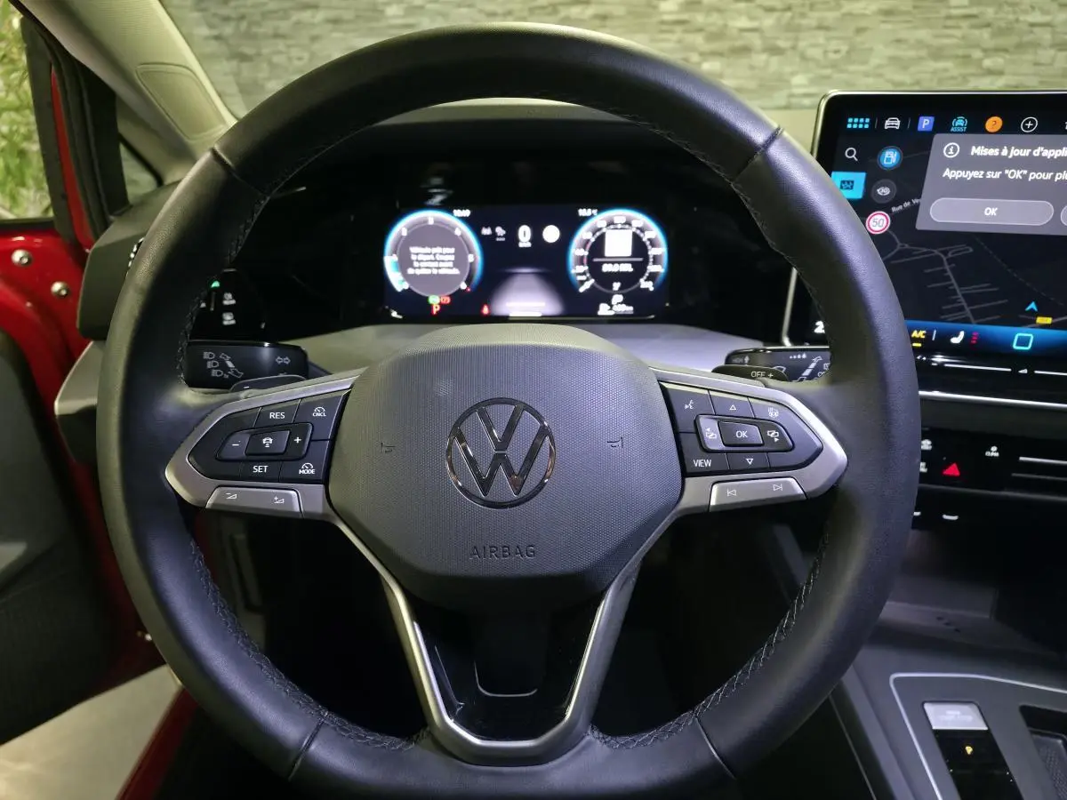 Vue rapprochée du volant noir de la Volkswagen Golf VIII rouge avec tableau de bord digital et écran tactile visible.