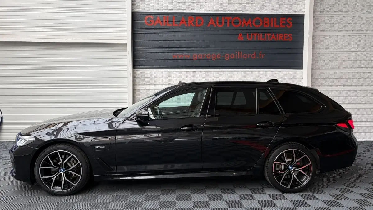 BMW Série 5 Touring 530e noir vue de profil côté gauche, avec jantes M Sport et prise de charge visible.