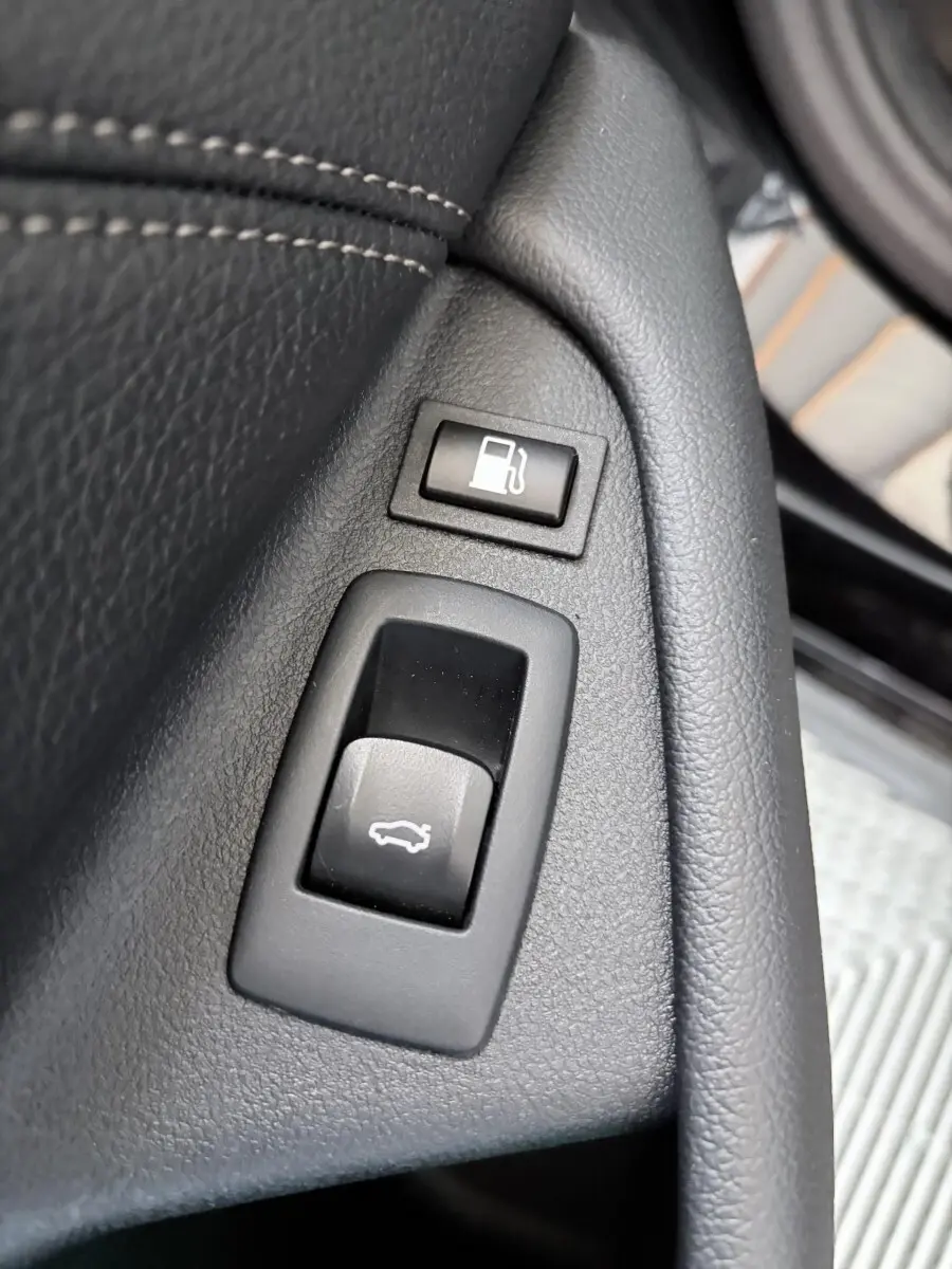 Gros plan sur les boutons d’ouverture du coffre et de la trappe à carburant dans l’habitacle noir d’une BMW Série 5 Touring 530e.