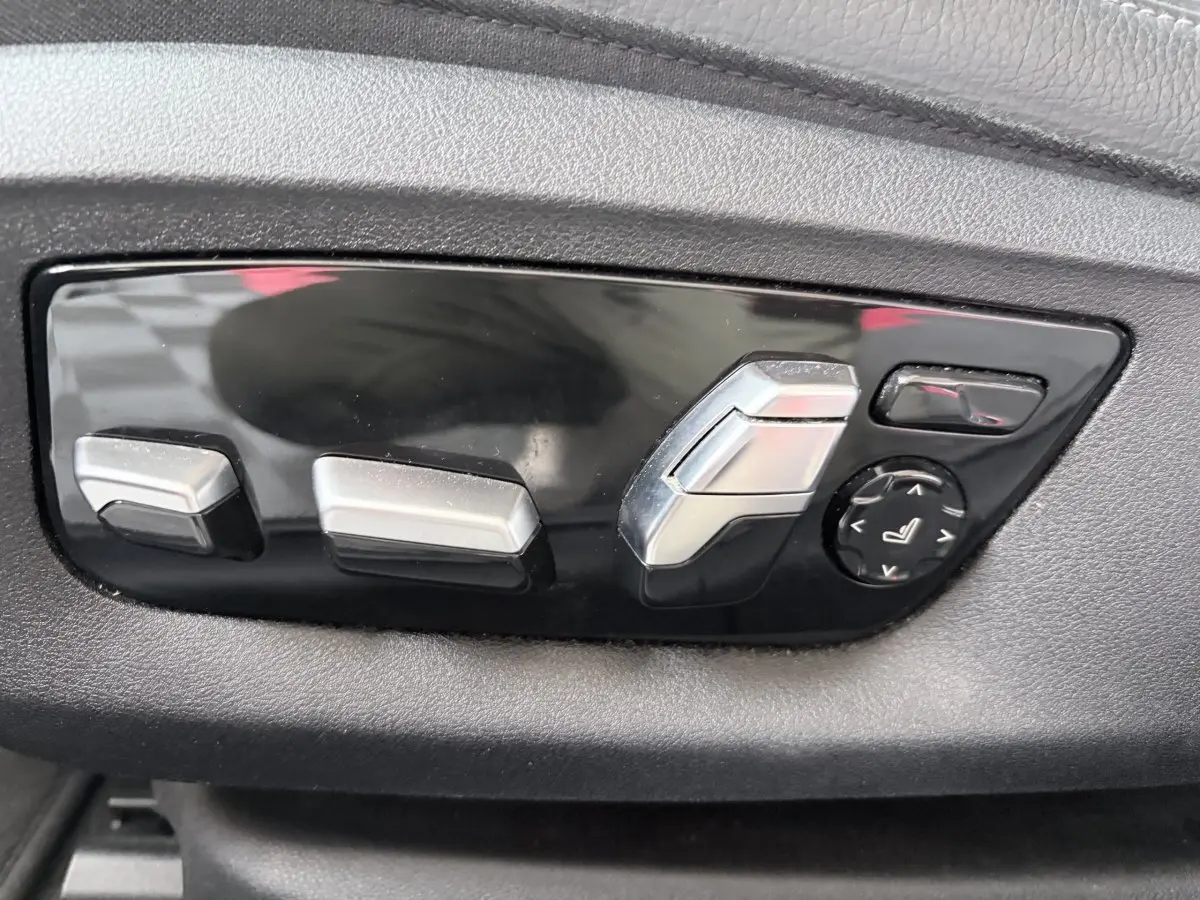 Gros plan sur les commandes de réglage électrique des sièges en plastique noir et argent dans une BMW Série 5 Touring noire.