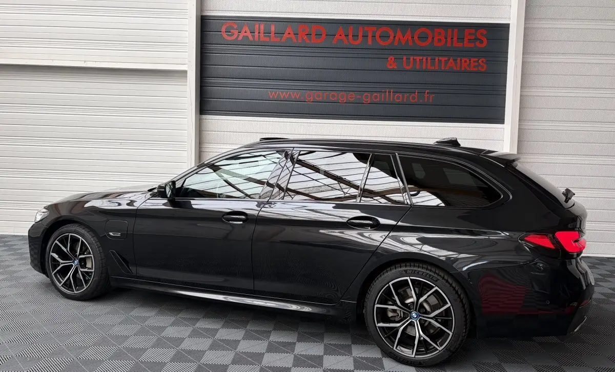 BMW Série 5 Touring 530e noire vue de profil côté gauche, avec jantes sport et vitres teintées.