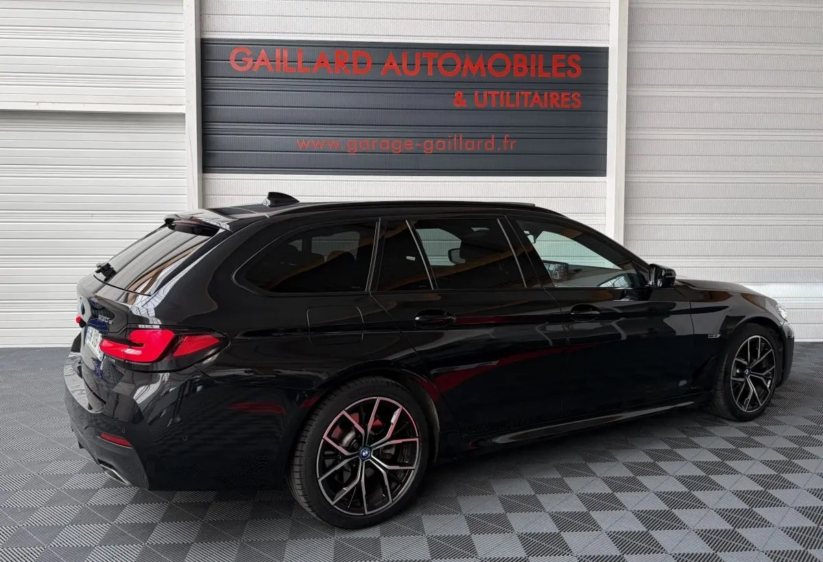 BMW Série 5 Touring 530e noire vue 3/4 arrière droit, avec jantes sport et vitres teintées.
