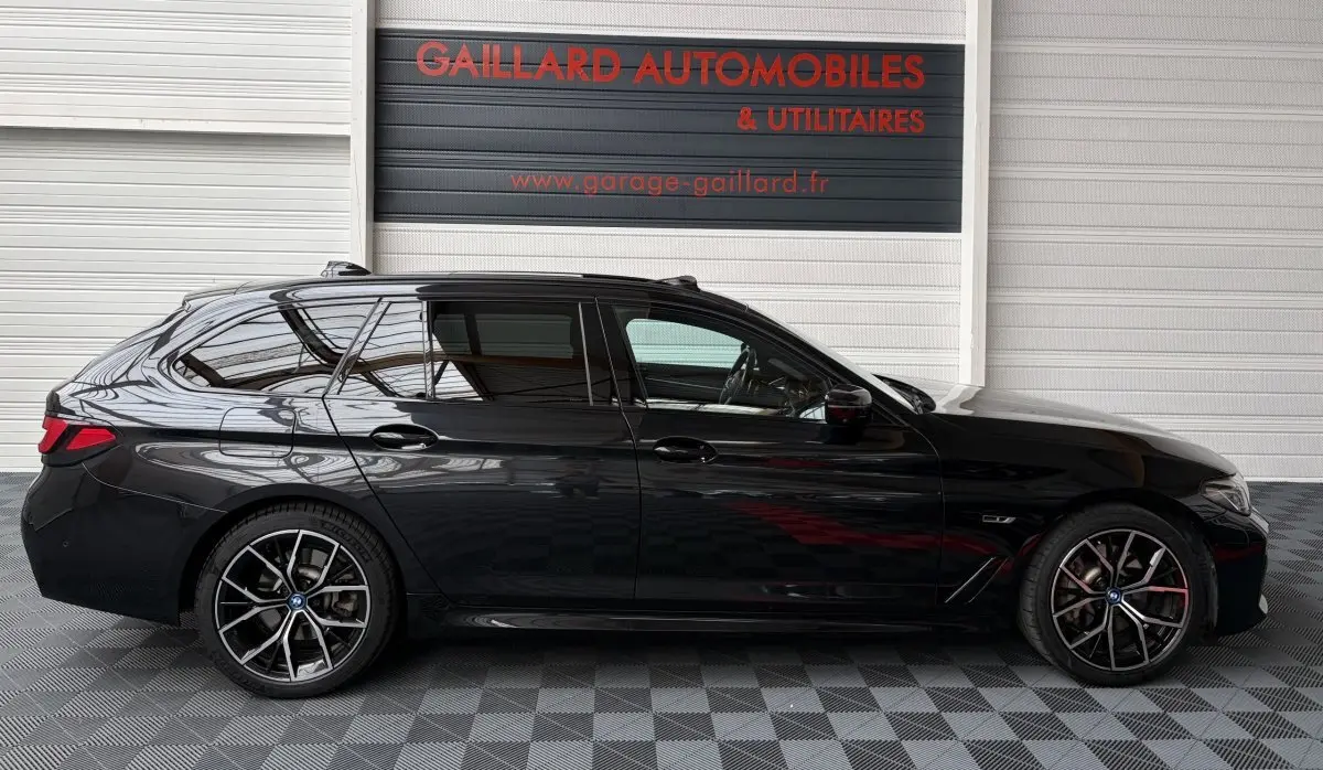 BMW Série 5 Touring 530e noire vue de profil côté gauche, avec jantes sport et vitres teintées.