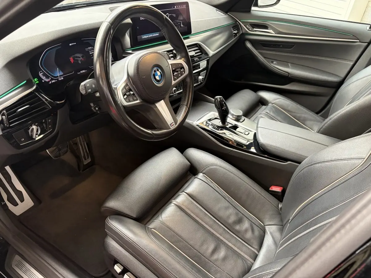 Vue intérieure côté conducteur de la BMW Série 5 Touring 530e noire, avec tableau de bord digital et sellerie cuir noire.
