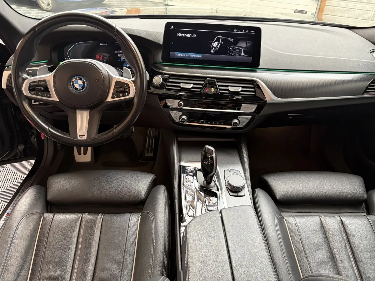 Vue intérieure avant de la BMW Série 5 Touring 530e noire, tableau de bord moderne avec écran tactile et volant M Sport.