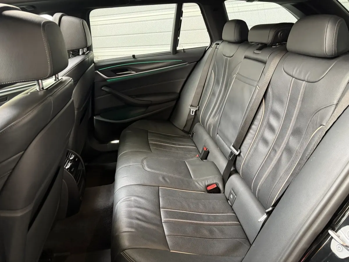 Vue intérieure arrière côté droit de la BMW Série 5 Touring 530e 2023 avec sièges cuir noirs et éclairage d'ambiance vert.