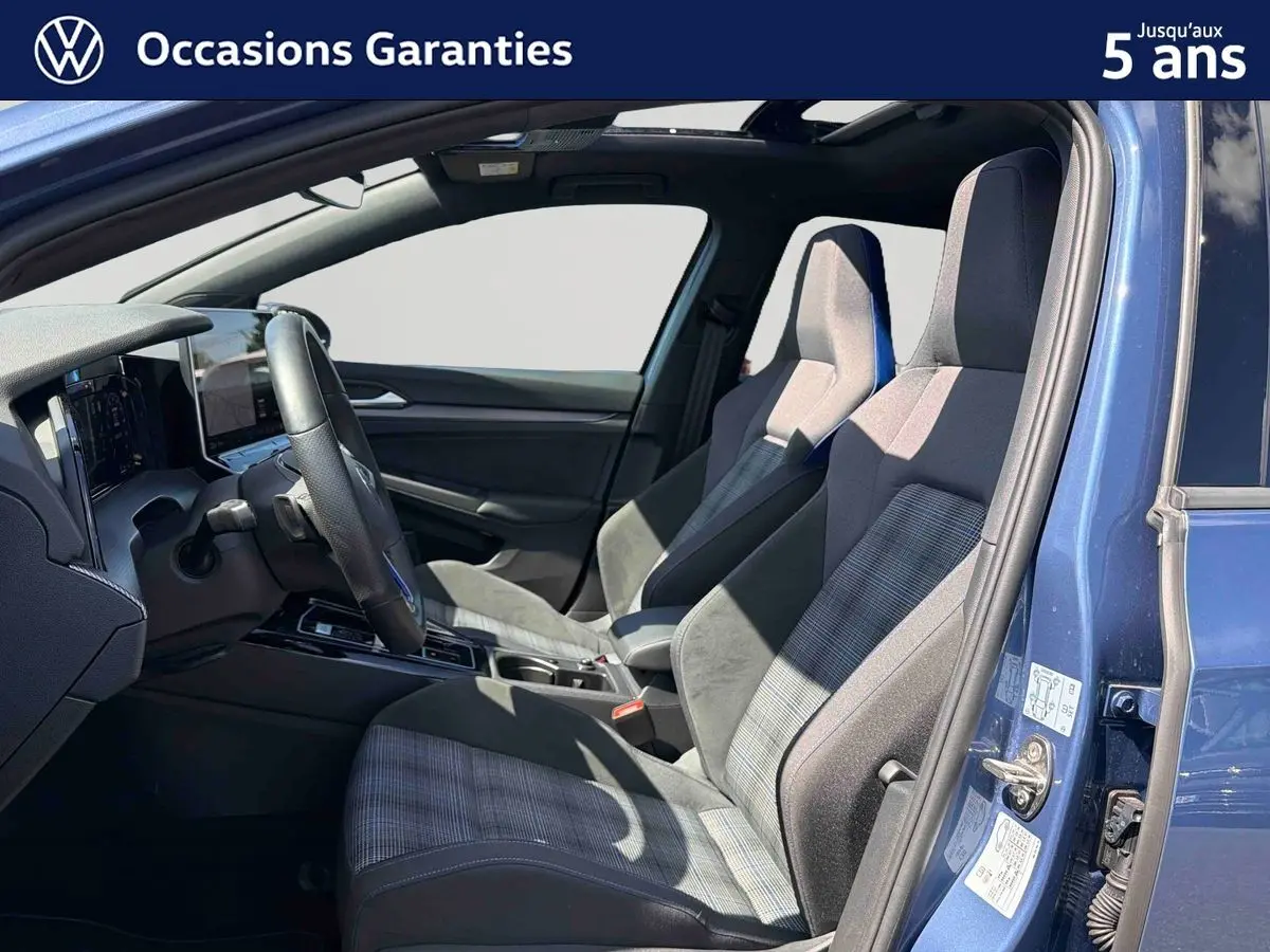 Vue intérieure côté gauche d'une Volkswagen Golf 1.5 eHybrid 2025 bleu, sièges sport haut de gamme avec tissu à motif écossais.