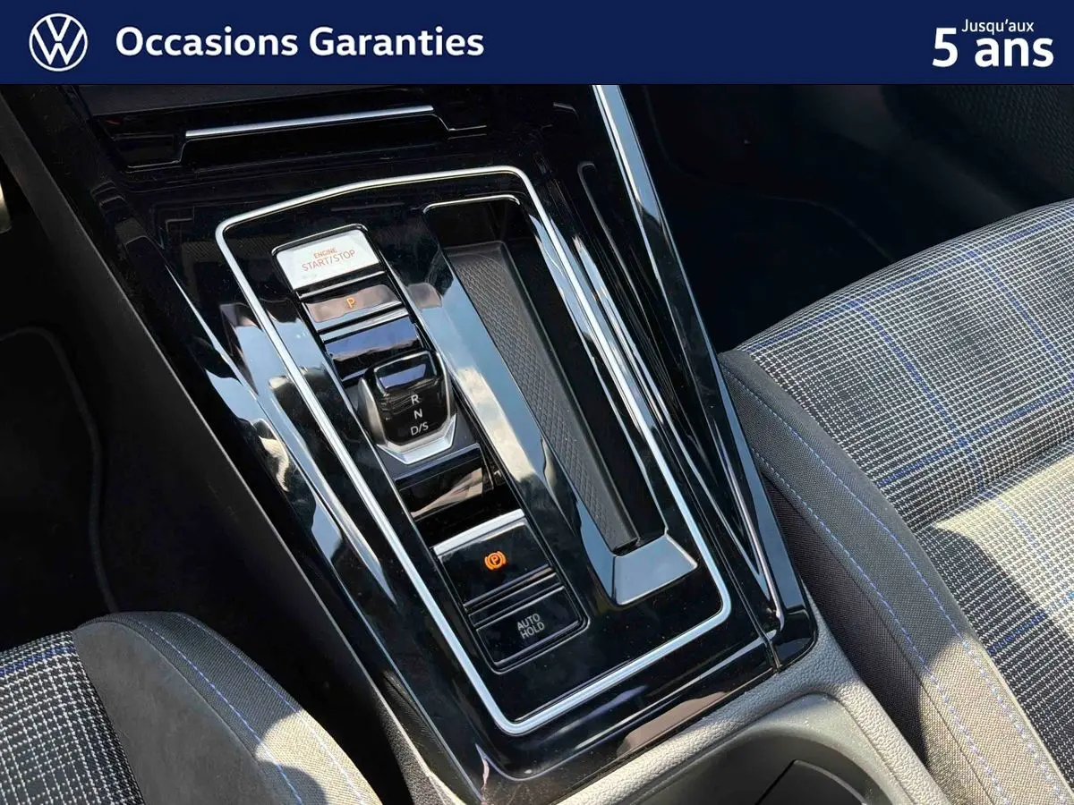 Gros plan sur la console centrale noire brillante et le siège avant à motif écossais bleu et gris de la Volkswagen Golf 1.5 eHybrid.