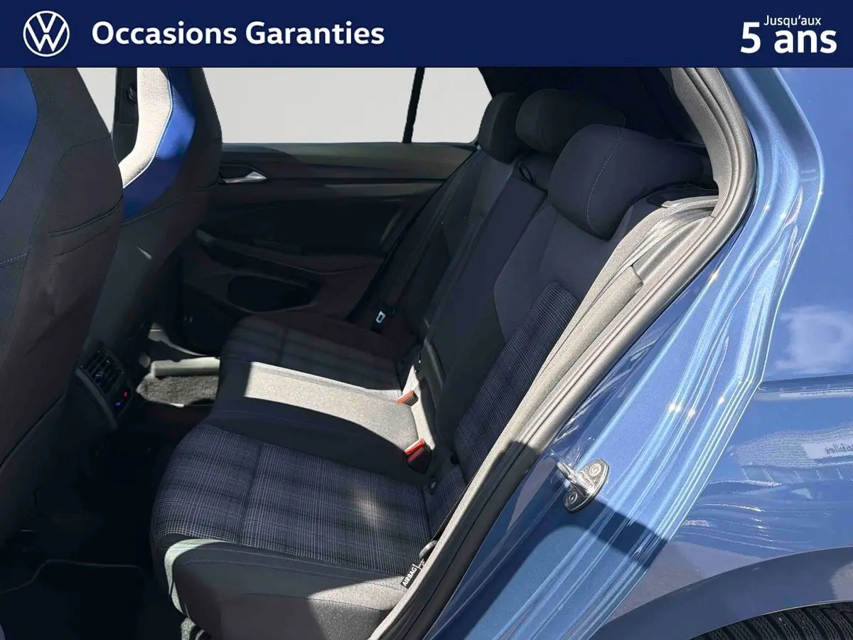 Vue côté arrière droit de l’habitacle bleu d’une Volkswagen Golf 1.5 eHybrid 2025, sièges arrière en tissu à motifs.